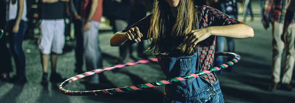 Girl wearing overalls with a black,pink,green striped hula hoop
