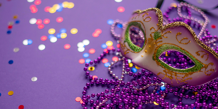 Mardi Gras mask lying on beads on a purple background