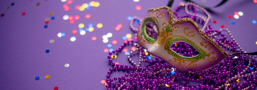 Mardi Gras mask lying on beads on a purple background